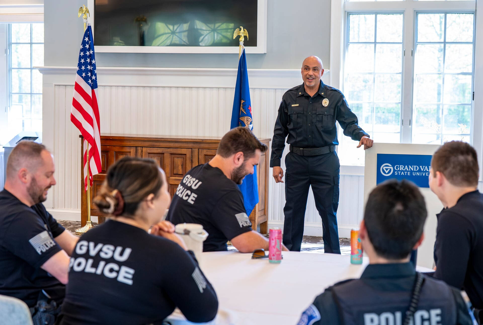 Daniel Lindstrom stands in the Alumni House in front of GVPD officers who are seated at round tables.